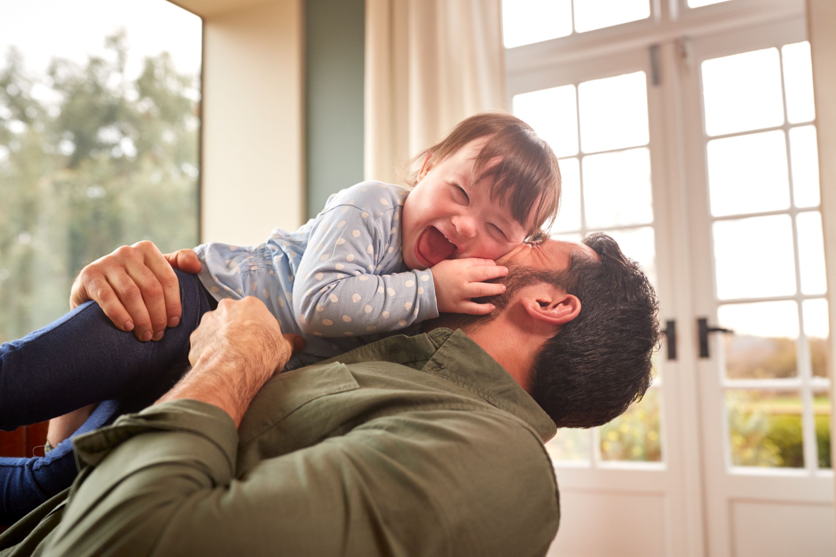 Loving Father Playing With Laughing Down Syndrome Daughter At Home Together